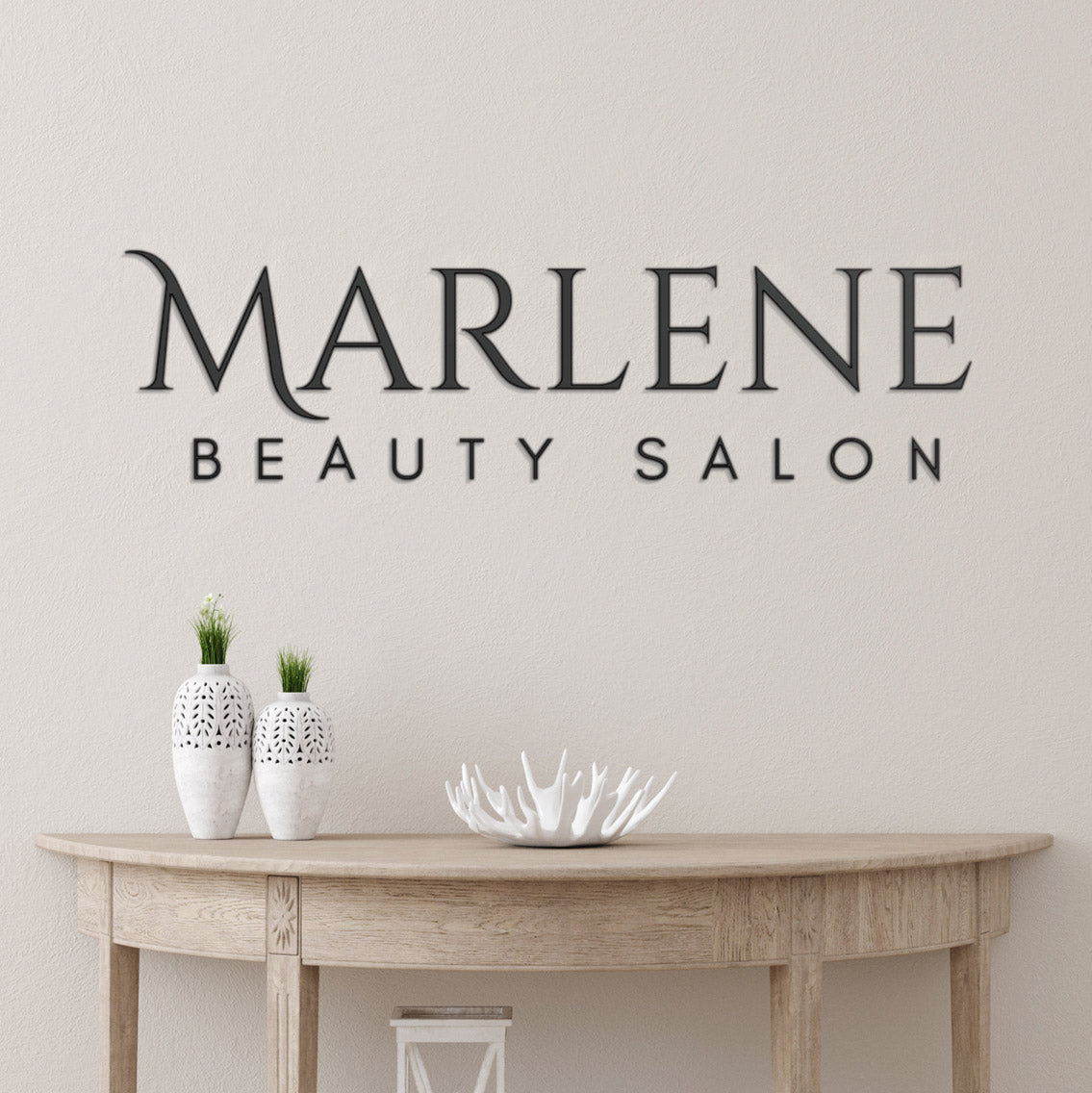 Marlene Beauty Salon matte black lobby logo on a wall above a sofa table with decorative items.