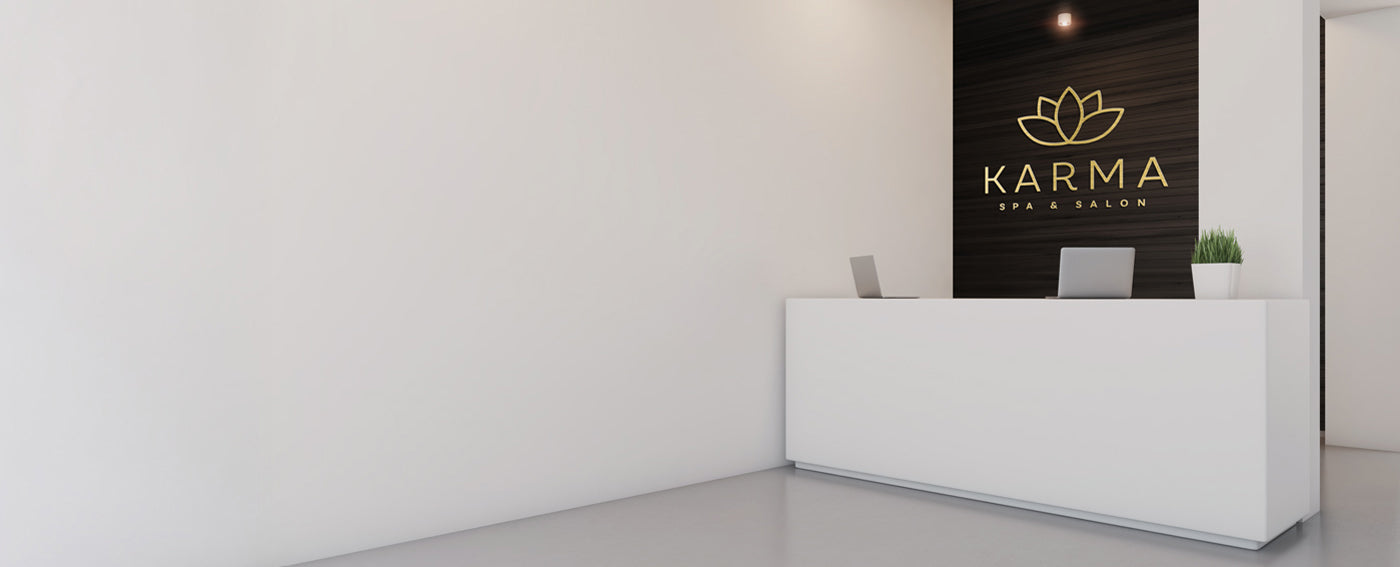 Modern interior with a white reception desk and 'Karma Spa & Salon' brushed gold lobby logo on a dark wall.